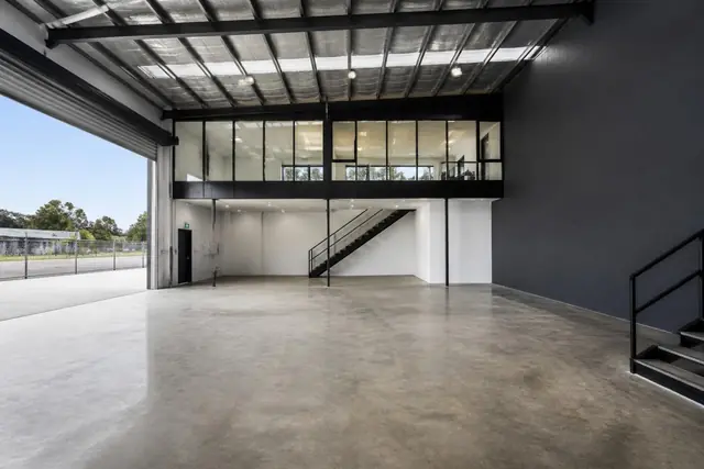 Inside a typical tenancy — sealed concrete slab, clear-span steel portal frame with up to 7.5m clearance, and the glazed mezzanine office above the entry.